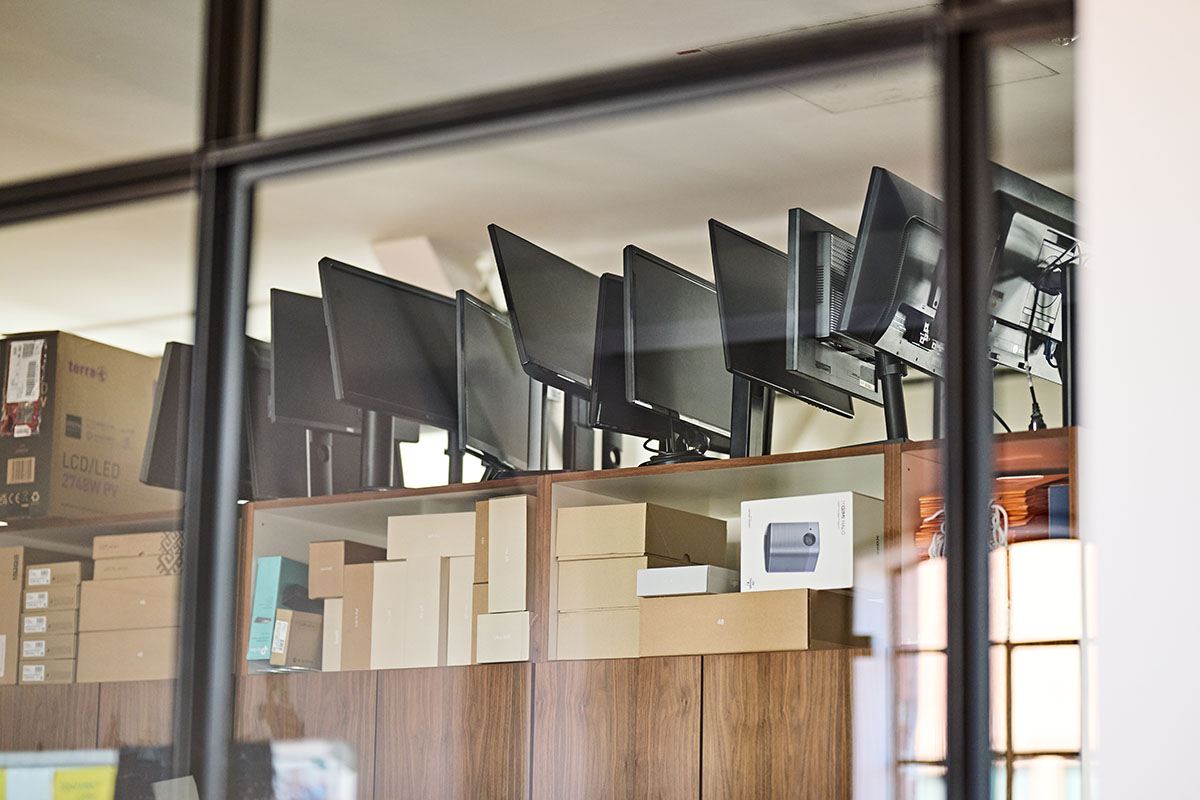 Blick durch eine Glasscheibe auf aufgereihte Monitore und IT-Hardware