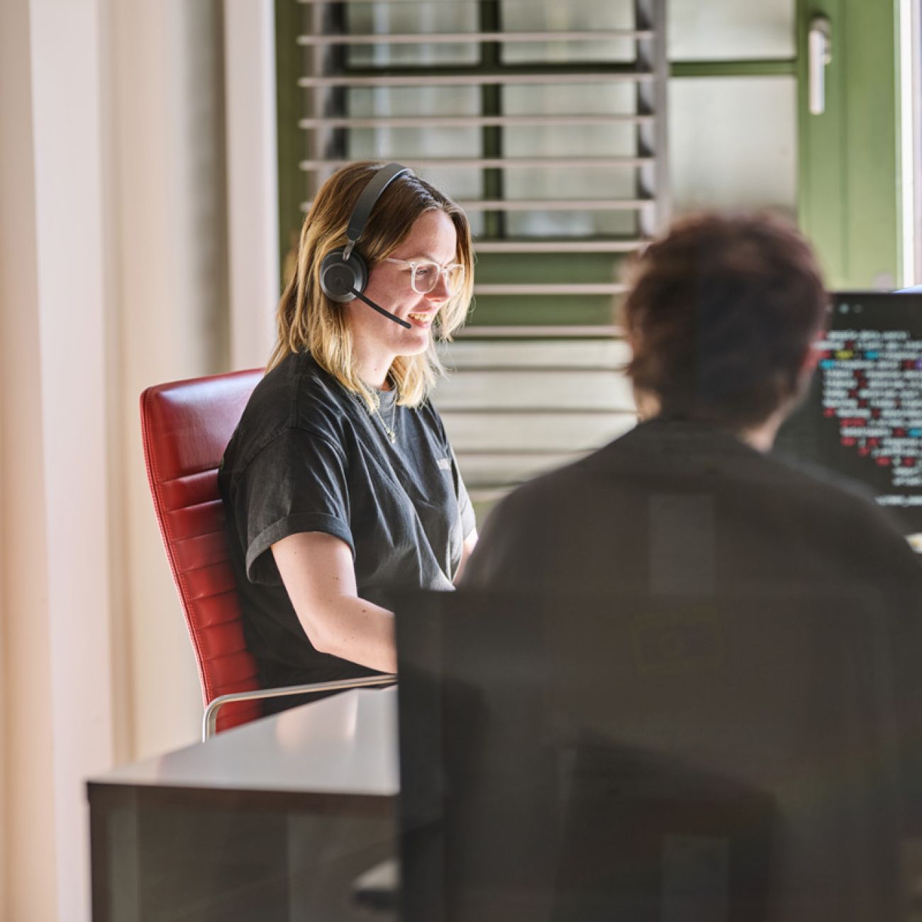 Eine soft-park-Mitarbeiterin mit Headset im IT-Support-Einsatz, im Hintergrund ein Bildschirm mit Code